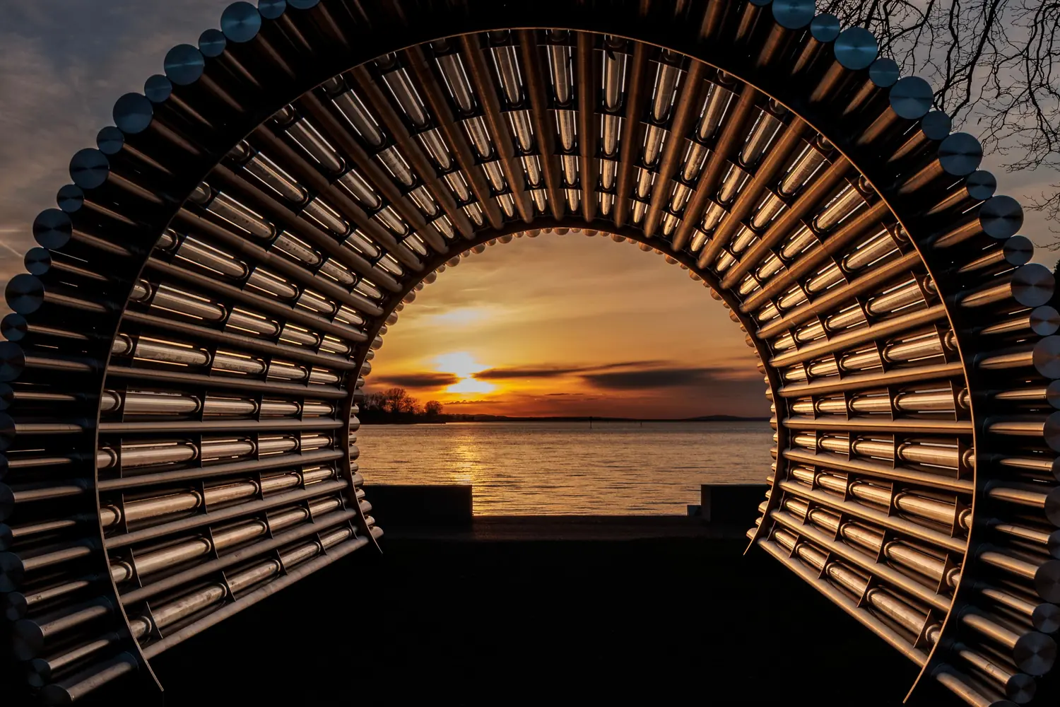 Ein bogenförmiges Bauwerk gibt den Blick auf einen Sonnenuntergang über dem Wasser frei